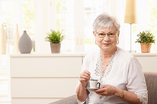 An elderly lady smiling whilst holding a cup of tea.